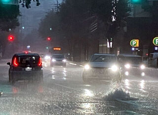 大雨で冠水した道路を走る車＝10日午後3時半ごろ、福岡県宗像市田久